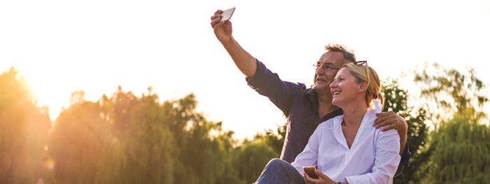 Man and woman taking a selfie at a park. Elements of financial well-being: present and future security and freedom of choice.