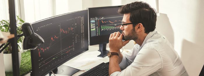 Man tracking financial developments on two computer monitors.