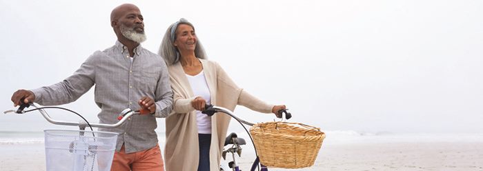 Man and woman walking their bikes along a beach.