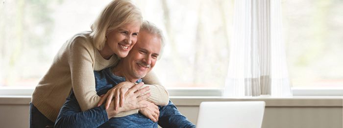 Woman hugs man as they both look at a laptop computer screen.