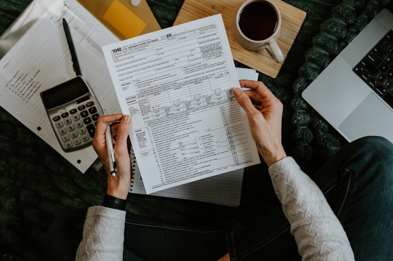 Hands holding tax forms with a calculator and laptop
